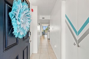 A hallway with a black door, a blue decorative item, and a kitchen area in the background. - Oceanfront 3BR Condo • Balcony Beach Views • Indoor Pool & Hot Tub (North Myrtle Beach)