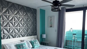 Una habitación de hotel moderna con una cama grande, un ventilador de techo y vistas al balcón exterior.