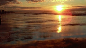 Atardecer sobre una playa mojada con reflejos del sol en el agua.