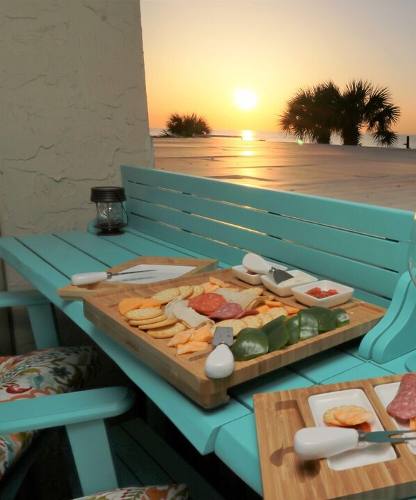 Enjoy a seaside dining experience with a beautifully set table featuring a selection of cheeses, meats, and fresh vegetables.