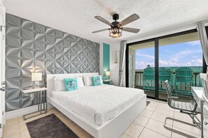 A hotel room with a bed, a nightstand, a ceiling fan, and a view of the outside. - Oceanfront 3BR Condo • Balcony Beach Views • Indoor Pool & Hot Tub (North Myrtle Beach)