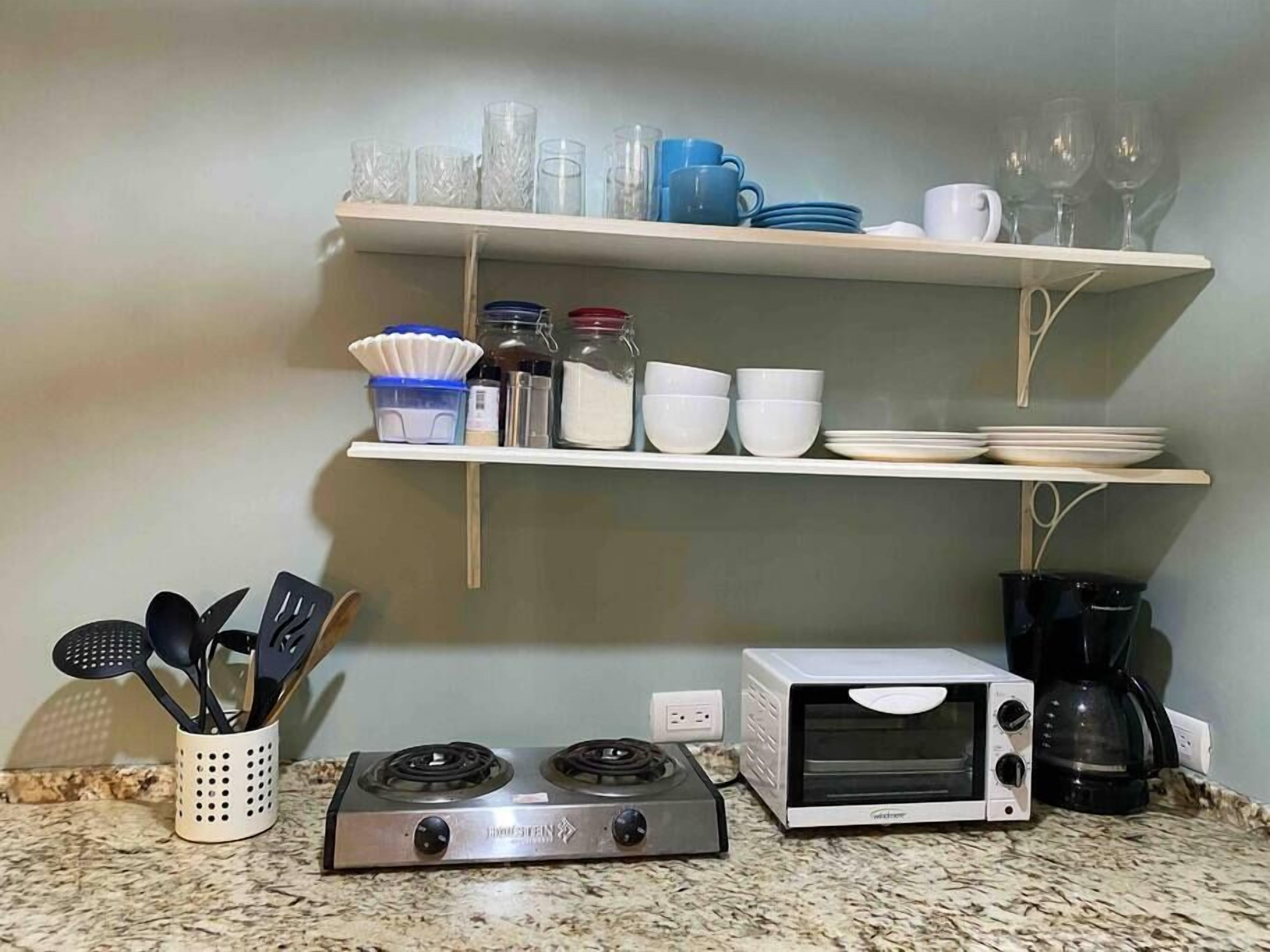 Una cocina con estufa a gas, microondas, cafetera y estantes con utensilios de cocina.