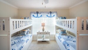 Une chambre avec deux lits superposés, une table de chevet avec une lampe et une fenêtre avec des stores.