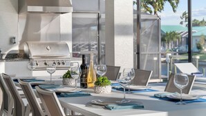 An outdoor dining area with a grill, wine glasses, and a view of palm trees. - Intervillas Florida - Villa Penelope (Cape Coral)
