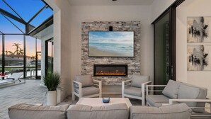 A modern outdoor living area with a stone wall, a flat-screen TV, and a fireplace. - Intervillas Florida - Villa Penelope (Cape Coral)