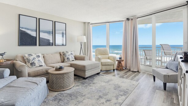 Een ruime woonkamer met een groot raam met uitzicht op het strand, een comfortabele zithoek en een ronde salontafel.