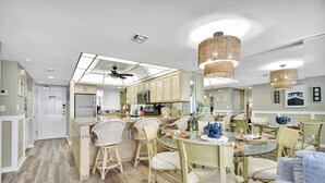 Een moderne keuken met een centraal eiland, barkrukken en een eethoek met ronde tafels en stoelen.