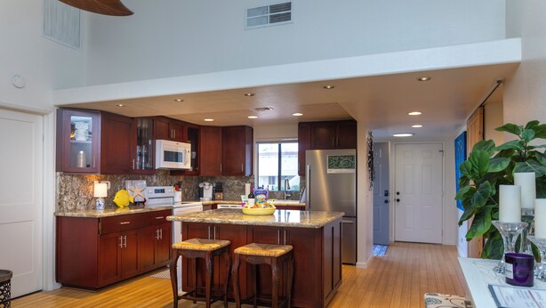 A spacious kitchen with wooden cabinets, a granite countertop, and a central island with stools. - Charming 2-bedroom condo with AC and WiFi in delightful Palm Desert (Palm Desert)