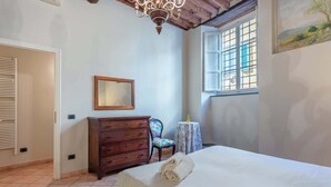 Una camera da letto con un letto, una cassettiera in legno, una sedia, un tavolino e una finestra con persiane.