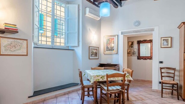 Zona pranzo con tavolo e sedie, una finestra con persiane e quadri appesi al muro.