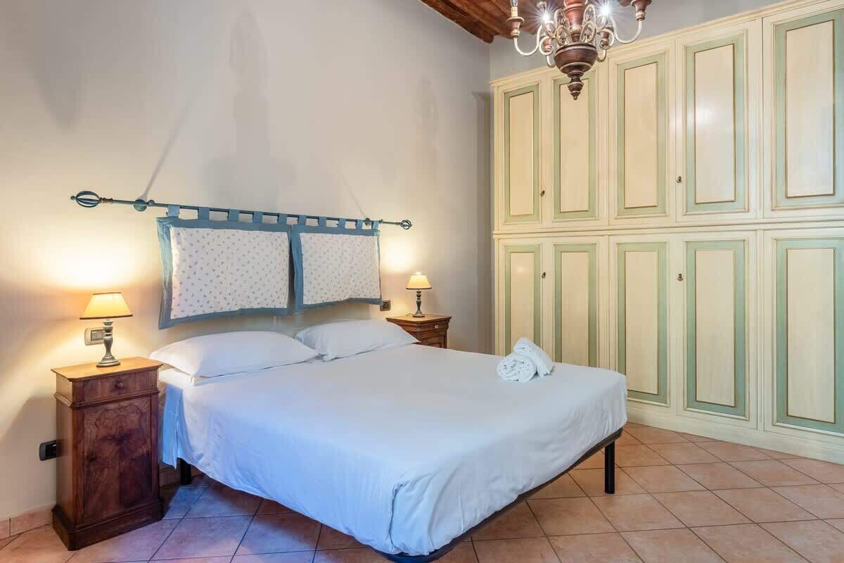 Une chambre à coucher comprenant un lit, deux tables de chevet avec des lampes, un lustre et une armoire à plusieurs portes.