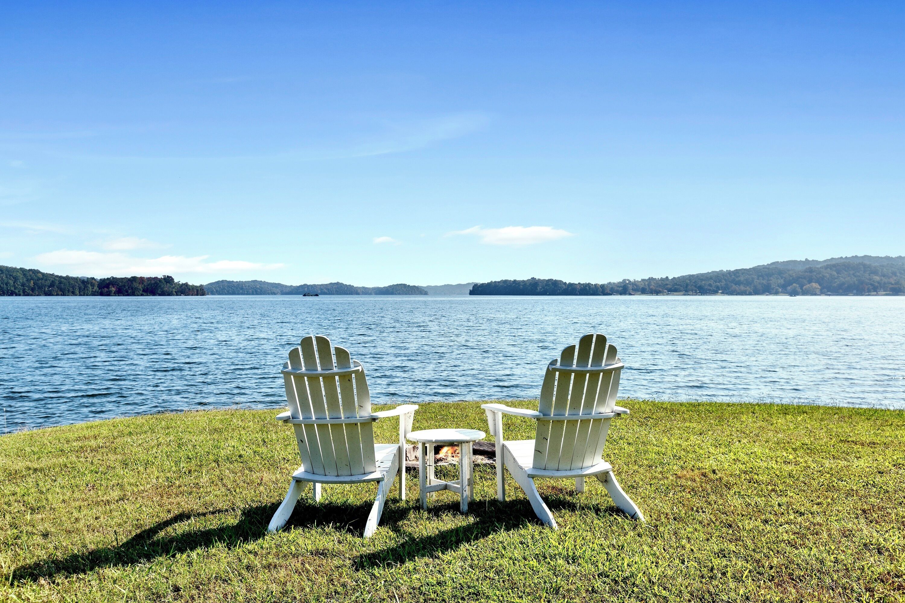 Zwei Adirondack-Stühle mit Blick auf einen See, dazwischen eine Rasenfläche.