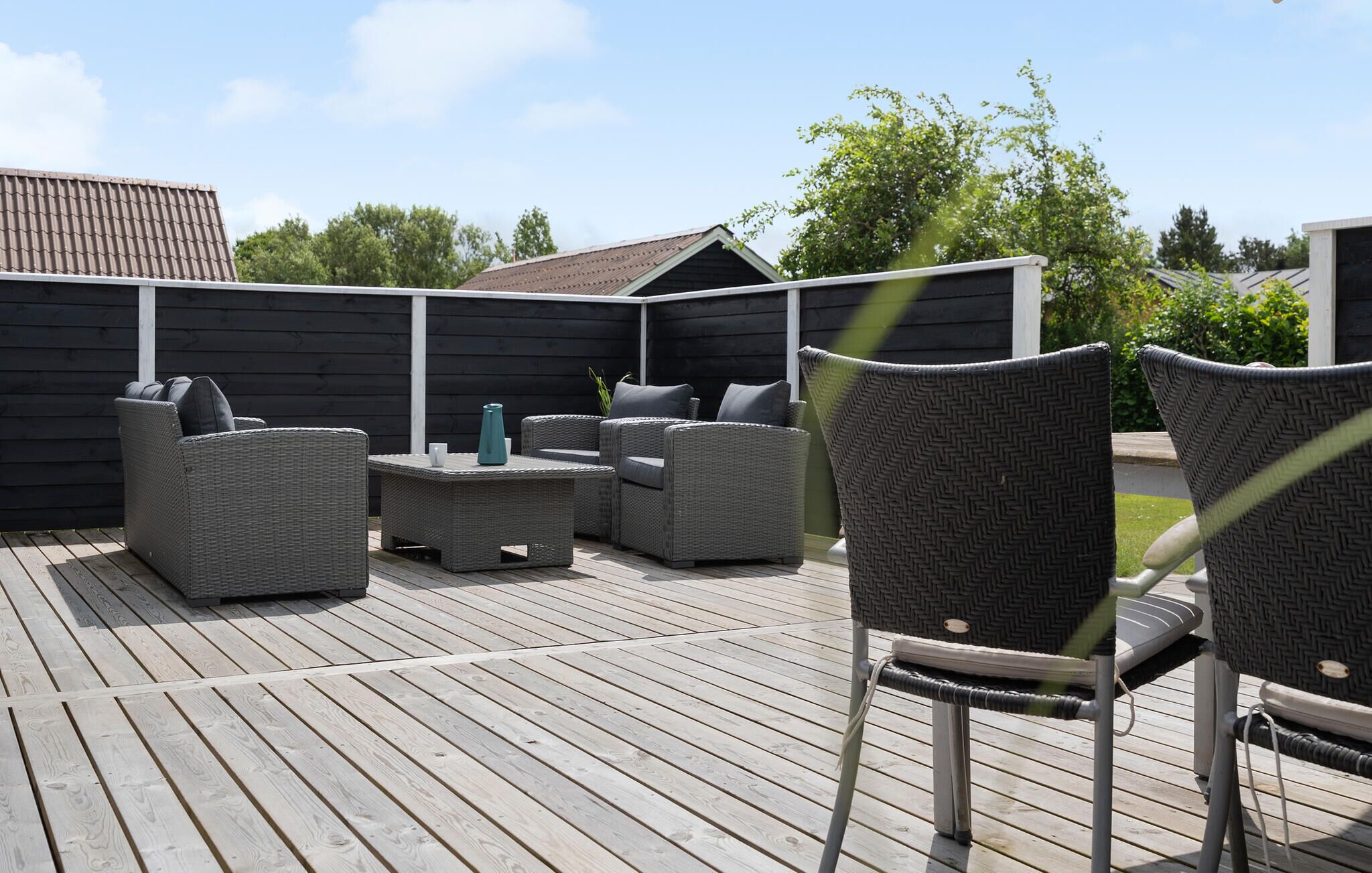 An outdoor patio with wicker furniture, a wooden deck, and a dark-colored fence.