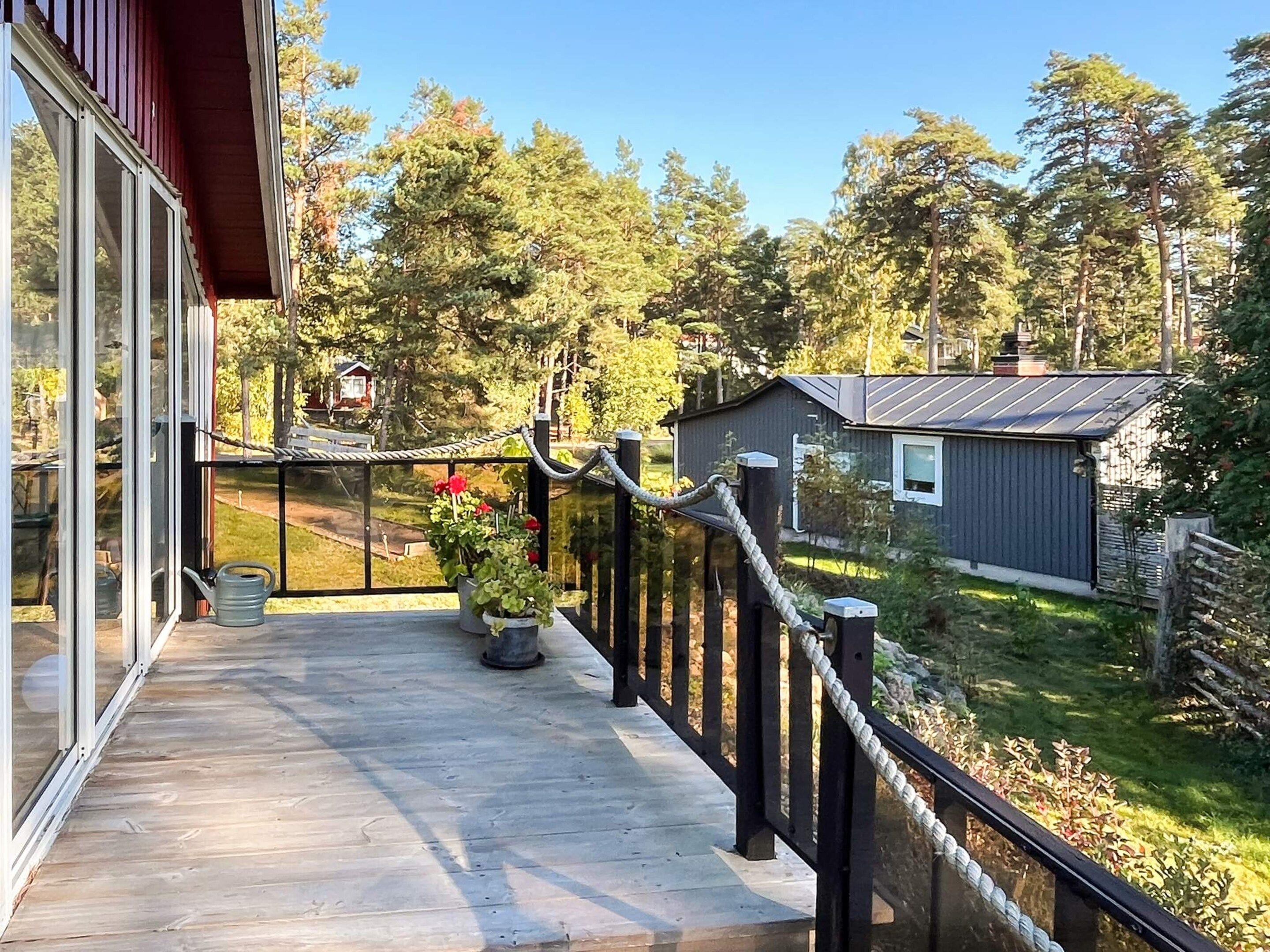 A wooden deck with a glass balustrade, a potted plant, and a metal watering can.