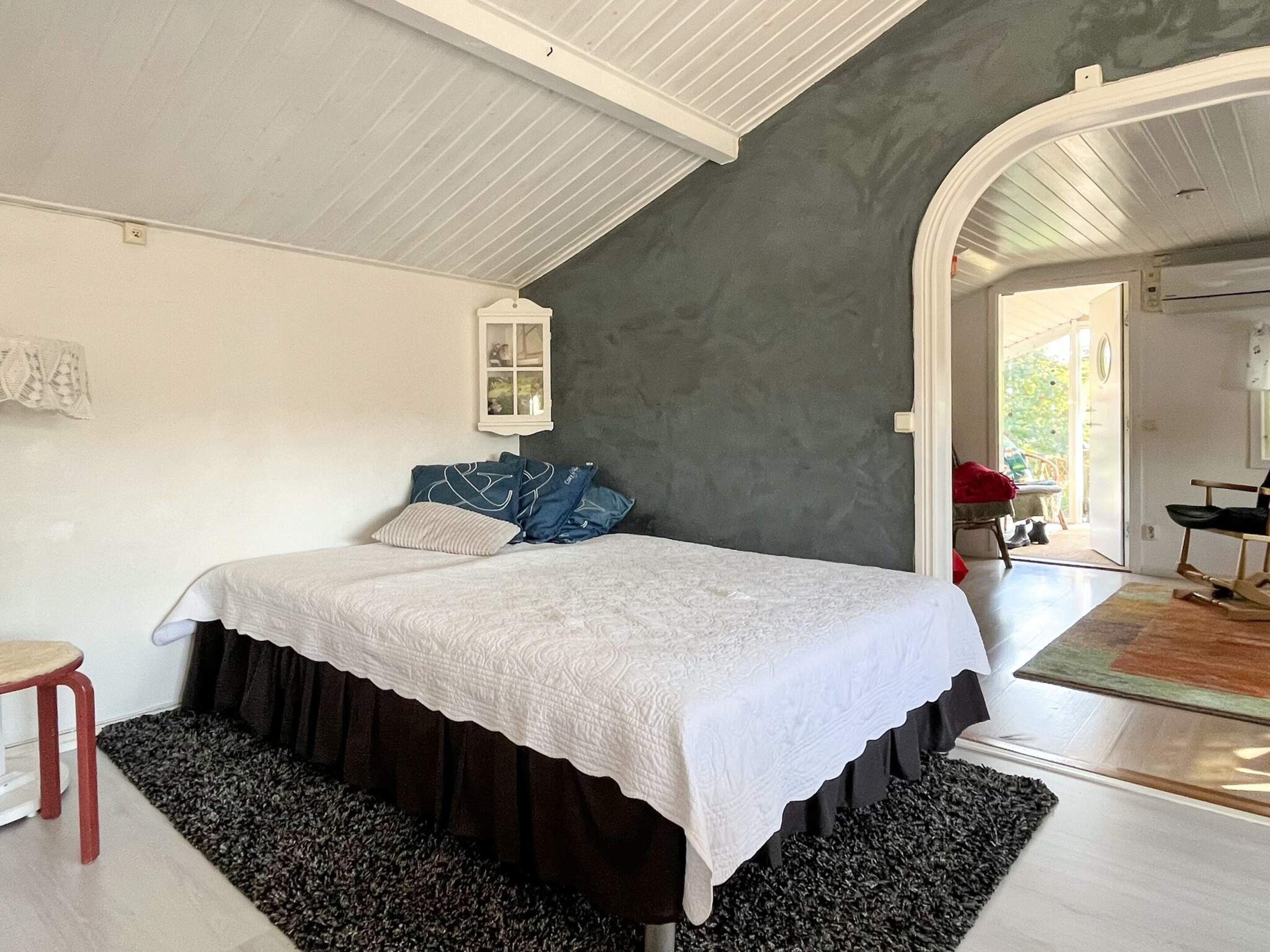 A bedroom with a bed, a small stool, a dark rug, a white wall, and a gray accent wall.