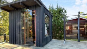 A modern wooden structure with a glass door, a wooden deck, and a metal fence. - 4 Person Holiday Home in Monsteras (Monsteras)