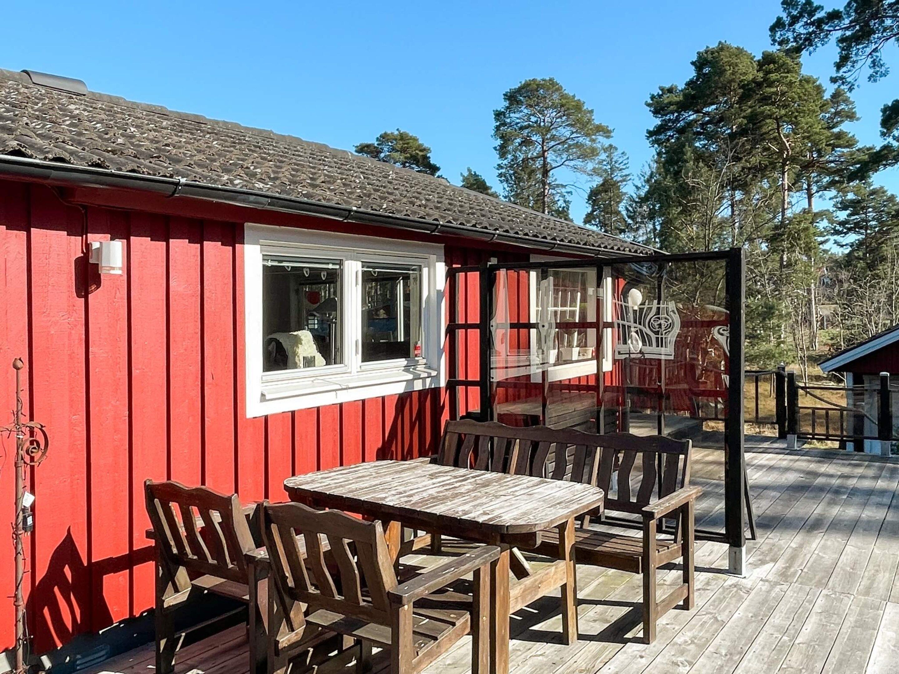A red building with a deck, wooden furniture, and a glass enclosure.