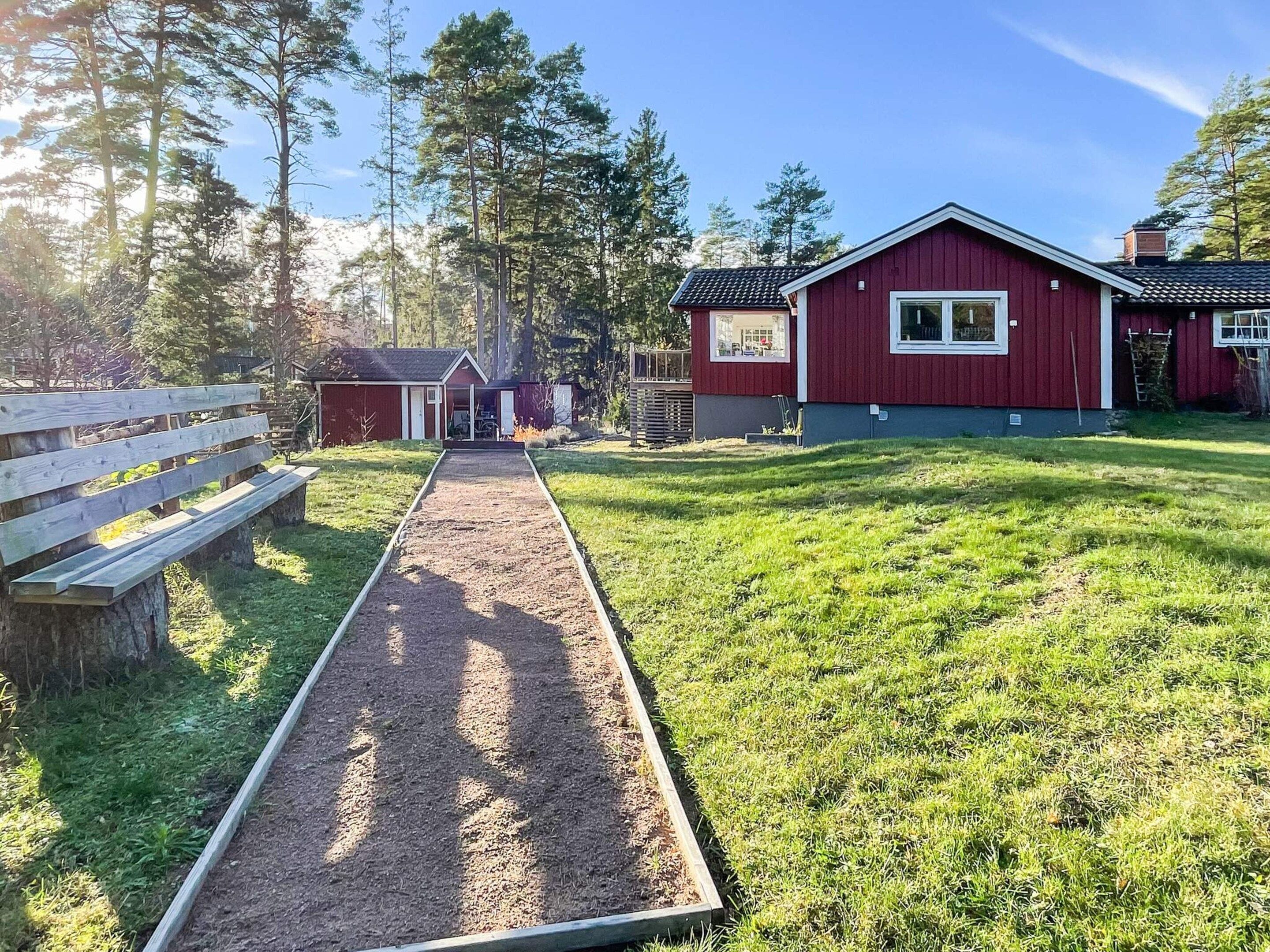 A red building with a wooden bench and a dirt path leading to it.