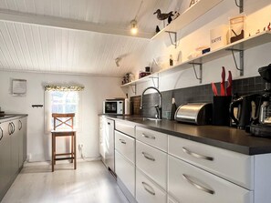 Una cocina con armarios blancos, microondas, hervidor y cafetera.