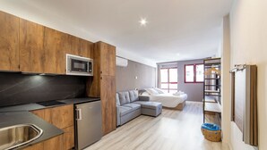A modern kitchen with a microwave, sink, and refrigerator. There is a gray sectional sofa in the living area and a small laundry basket. - Albufera Dreams Nature Suites (Valencia)
