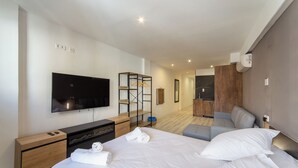A modern hotel room with a large bed, a flat-screen TV, a wooden dresser, and a seating area with a sofa and armchairs. - Albufera Dreams Nature Suites (Valencia)
