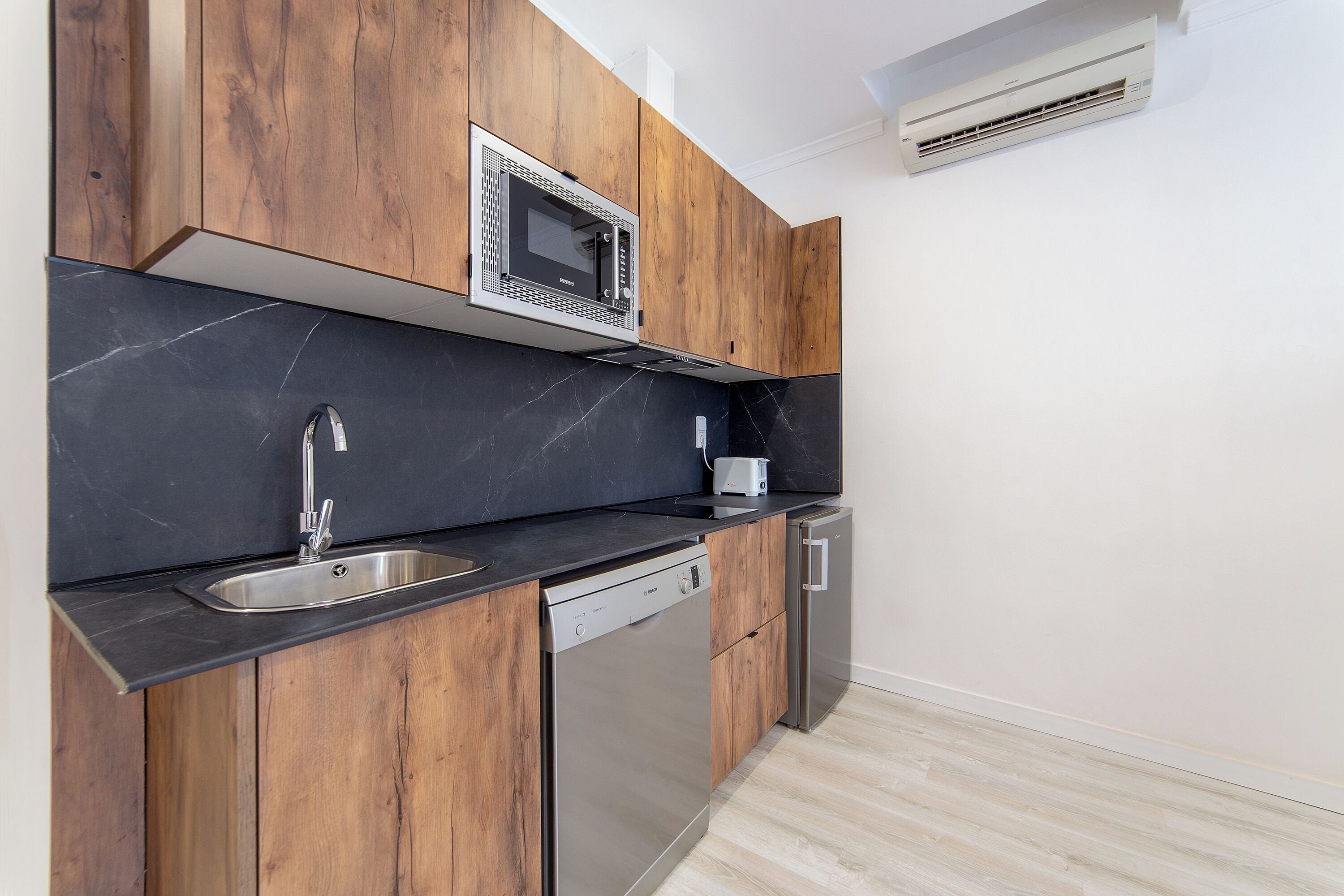 Een moderne keuken met houten kastjes, een ingebouwde magnetron, een vaatwasser en een roestvrijstalen spoelbak.