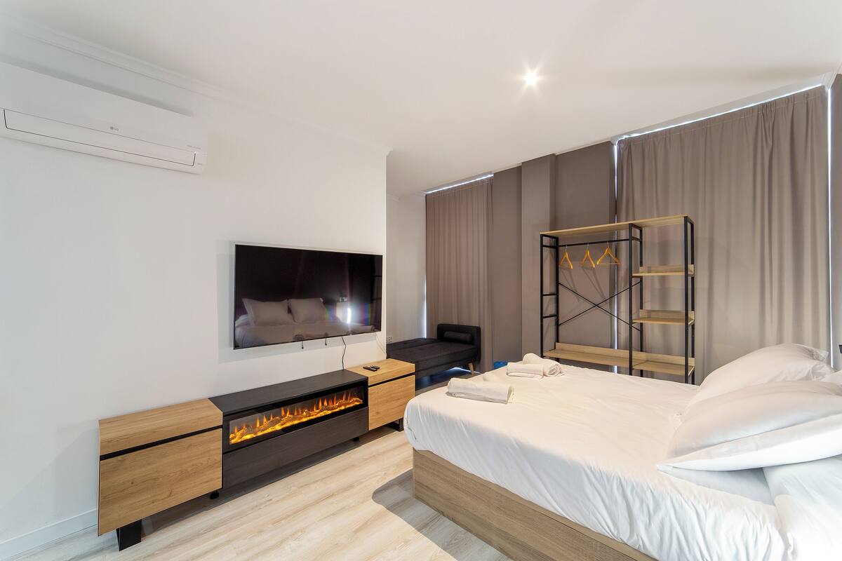 A modern bedroom with a TV, a built-in fireplace, a bed, and a wooden ladder shelf.