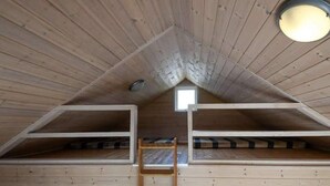 Eine Holzhütte mit Schlafbereich im Loft-Stil, einem kleinen Fenster und einer Leiter zum Loft.