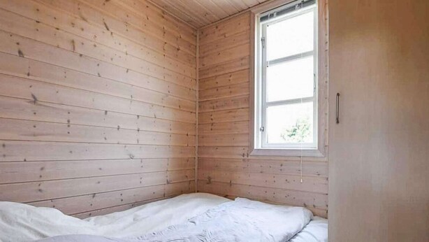 Een kleine kamer met een enkel bed, houten wanden en een raam.
