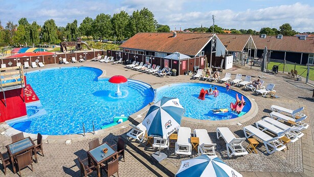 Ein Schwimmbecken mit mehreren Bahnen, Liegestühlen und Sonnenschirmen.