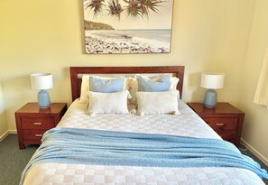 Un lit bien fait, recouvert d’une couvre-lit à carreaux, deux tables de chevet avec des lampes et une décoration murale sur le thème de la plage.