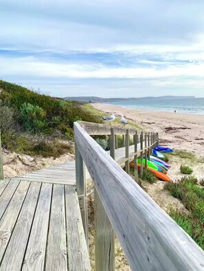 Une promenade en bois mène à une plage où sont alignés des kayaks aux couleurs vives.