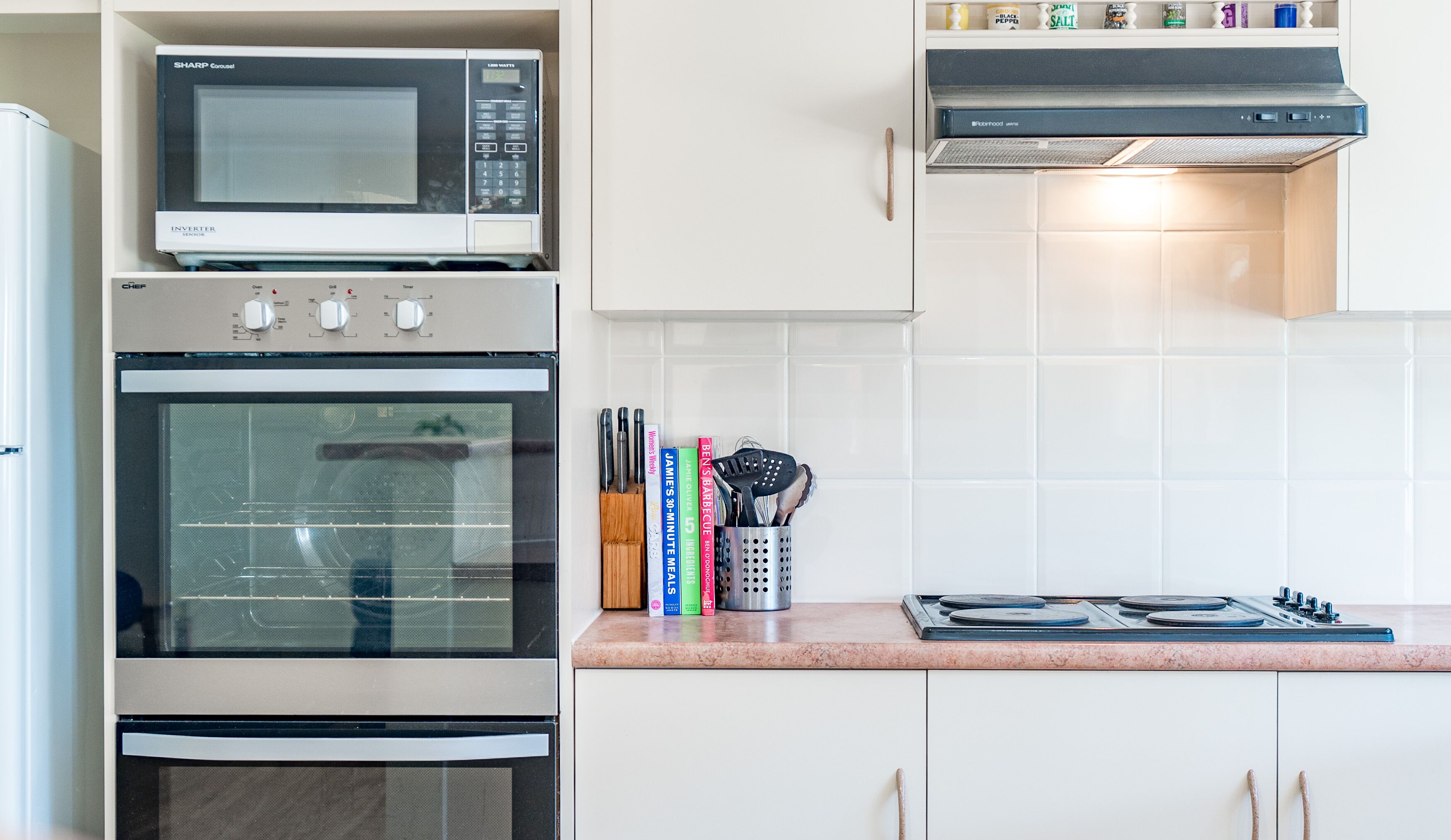 Una cocina equipada con microondas, horno, estufa y un mueble con especias, libros y utensilios.