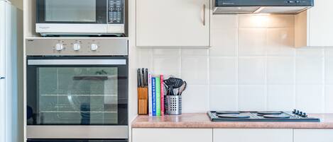 Una cocina equipada con microondas, horno, estufa y un mueble con especias, libros y utensilios.