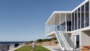 Ein modernes Gebäude mit Glasfassade, einer Rasenfläche und einer Treppe, die zu einer oberen Ebene führt.