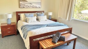 Ein Schlafzimmer mit einem Bett, Nachttischen, einer Bank und einem Fenster mit Vorhängen.