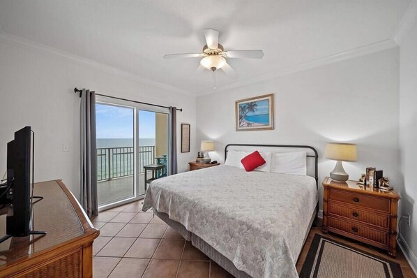 A hotel room with a bed, a TV, a balcony with a view, and a ceiling fan.