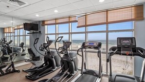 Ein Fitnessstudio mit Laufbändern, Crosstrainern und einem Fahrradergometer mit Blick auf einen Strand.