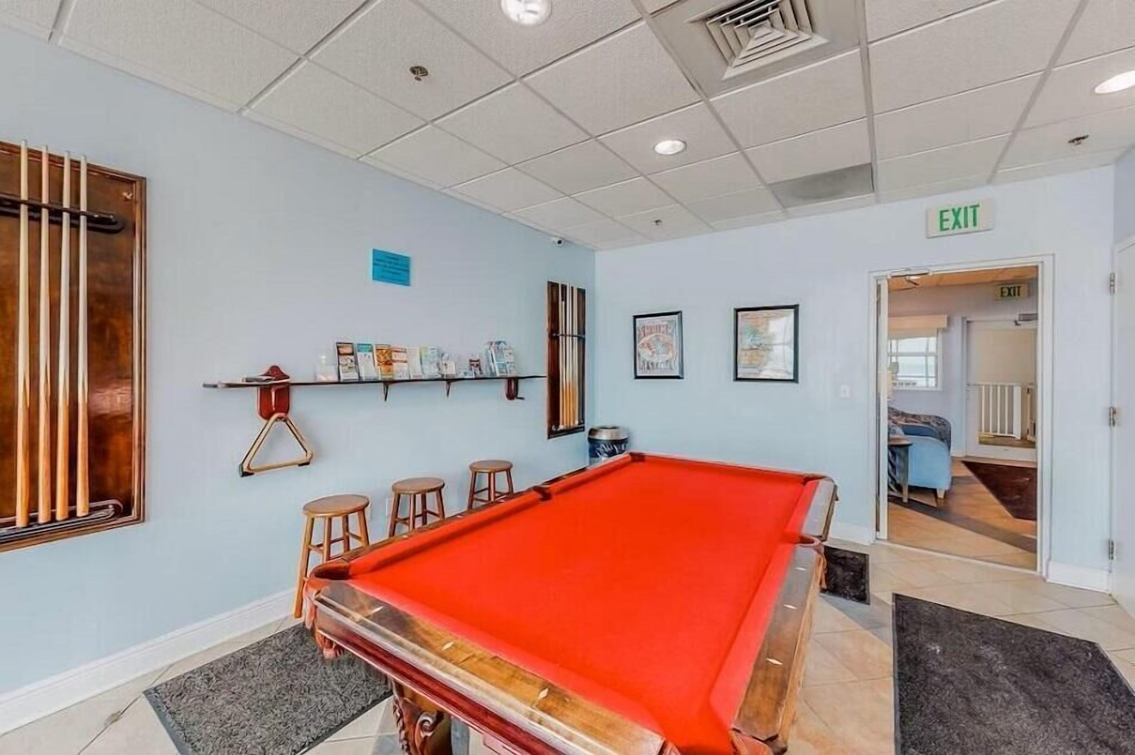 Une table de billard dans une pièce aux murs bleu clair, avec un panneau indiquant la sortie et une porte menant à une autre pièce.