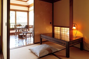 Una habitación japonesa tradicional con suelo de tatami, una cama de madera baja, un almohadón, una mesa y una lámpara.