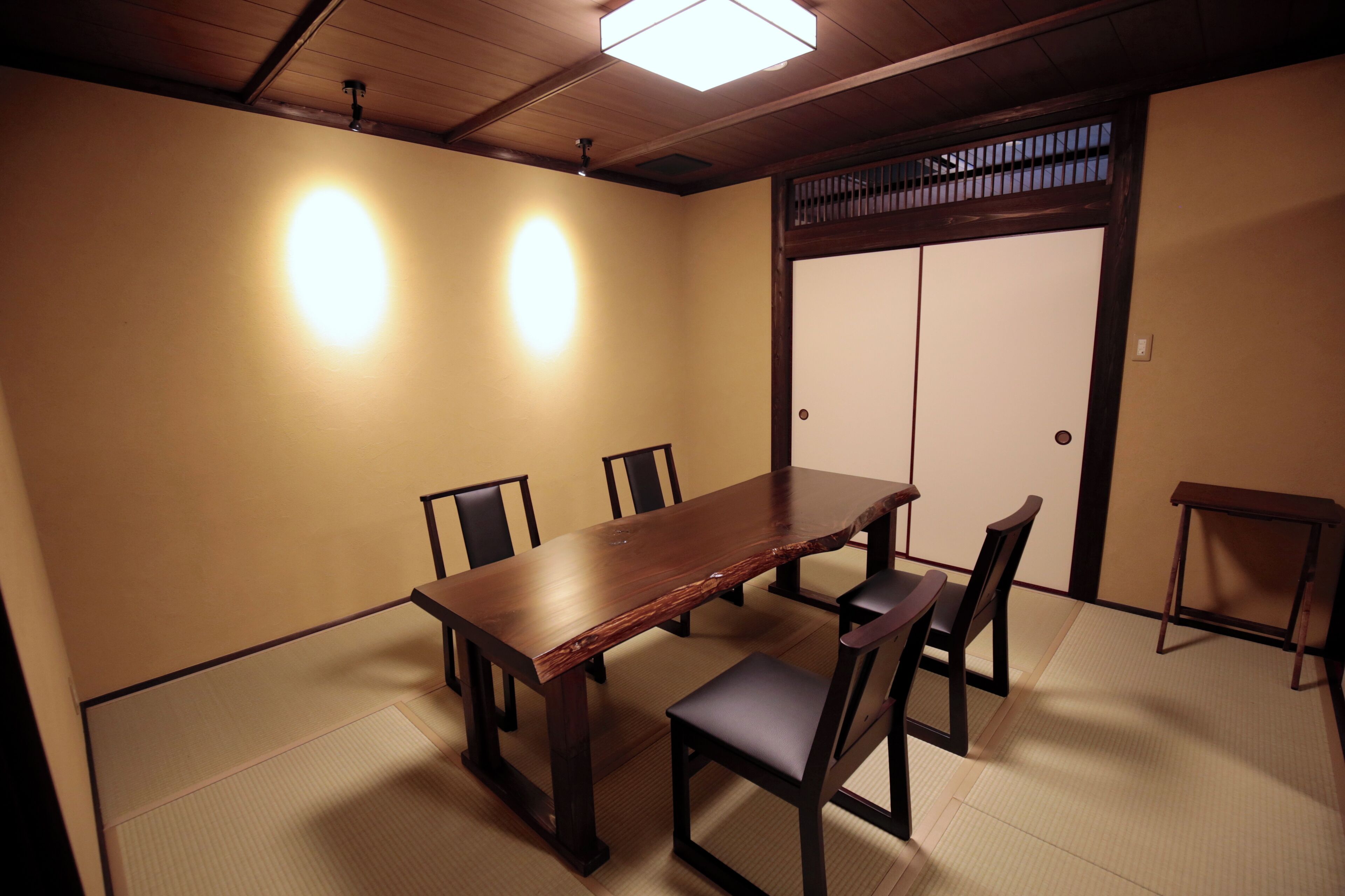 A traditional Japanese-style room with tatami flooring, a wooden table, and chairs.