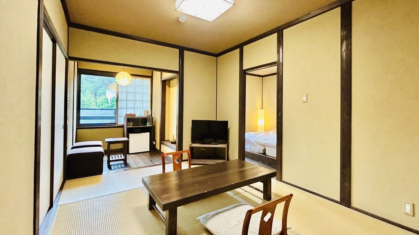 Ein traditioneller japanischer Raum mit Tatami-Böden, einem niedrigen Tisch, einem Fernseher und einem Bett.