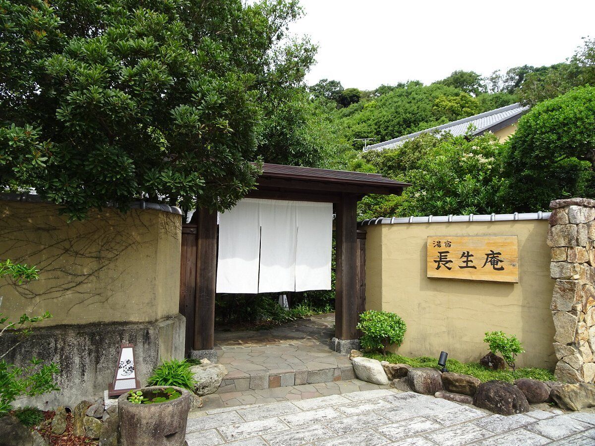 A traditional Japanese entrance with a wooden gate, a stone wall, and a sign with Japanese characters.