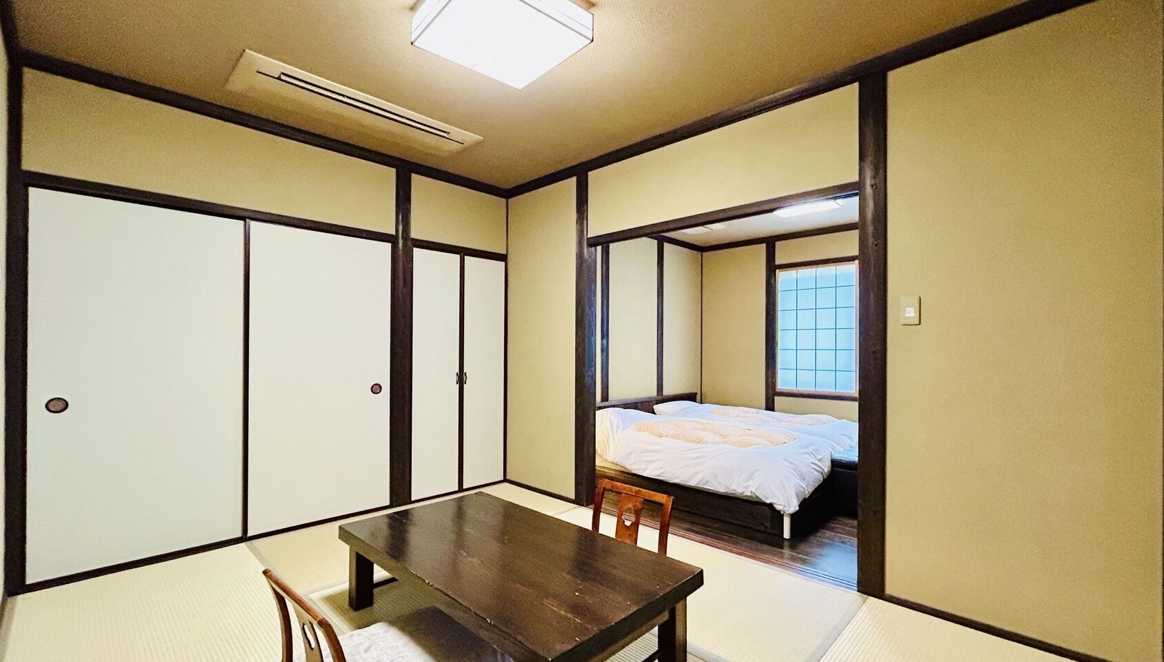 Ein traditioneller japanischer Raum mit Tatami-Boden, einem niedrigen Holztisch und einem Bett mit Futon.