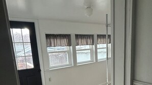 Ein Zimmer mit Holzboden, einem schwarzen Mülleimer und einer Tür zu einem anderen Raum.