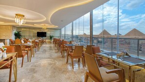 A spacious dining area with modern furnishings and large windows offering a view of pyramids. - Pyramids Plateau Hotel (Giza)