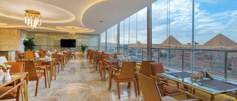 A spacious dining area with modern furnishings and large windows offering a view of pyramids.