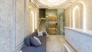 A modern lobby with a marble reception desk, a grey sofa with patterned cushions, and a staircase leading to an elevator. - Pyramids Plateau Hotel (Giza)