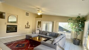 A living room with a grey sofa, a coffee table, and a red rug. There is a ceiling fan, a potted plant, and a window with a view. - Spacious Pet-Friendly Home w/Fenced Yard & Central (Prescott)