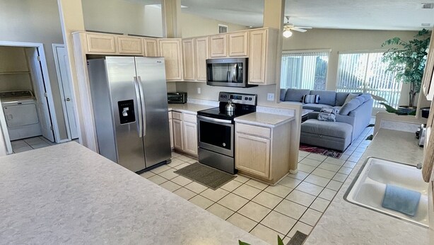 A modern kitchen with a refrigerator, microwave, stove, and sink. There is a dining area with a sofa and a large window. - Spacious Pet-Friendly Home w/Fenced Yard & Central (Prescott)